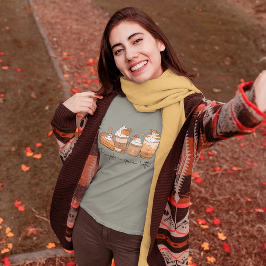 Smiling woman wearing a sage green t-shirt with illustrated pumpkin spice lattes and fall-themed designs while outdoors in autumn scenery. 