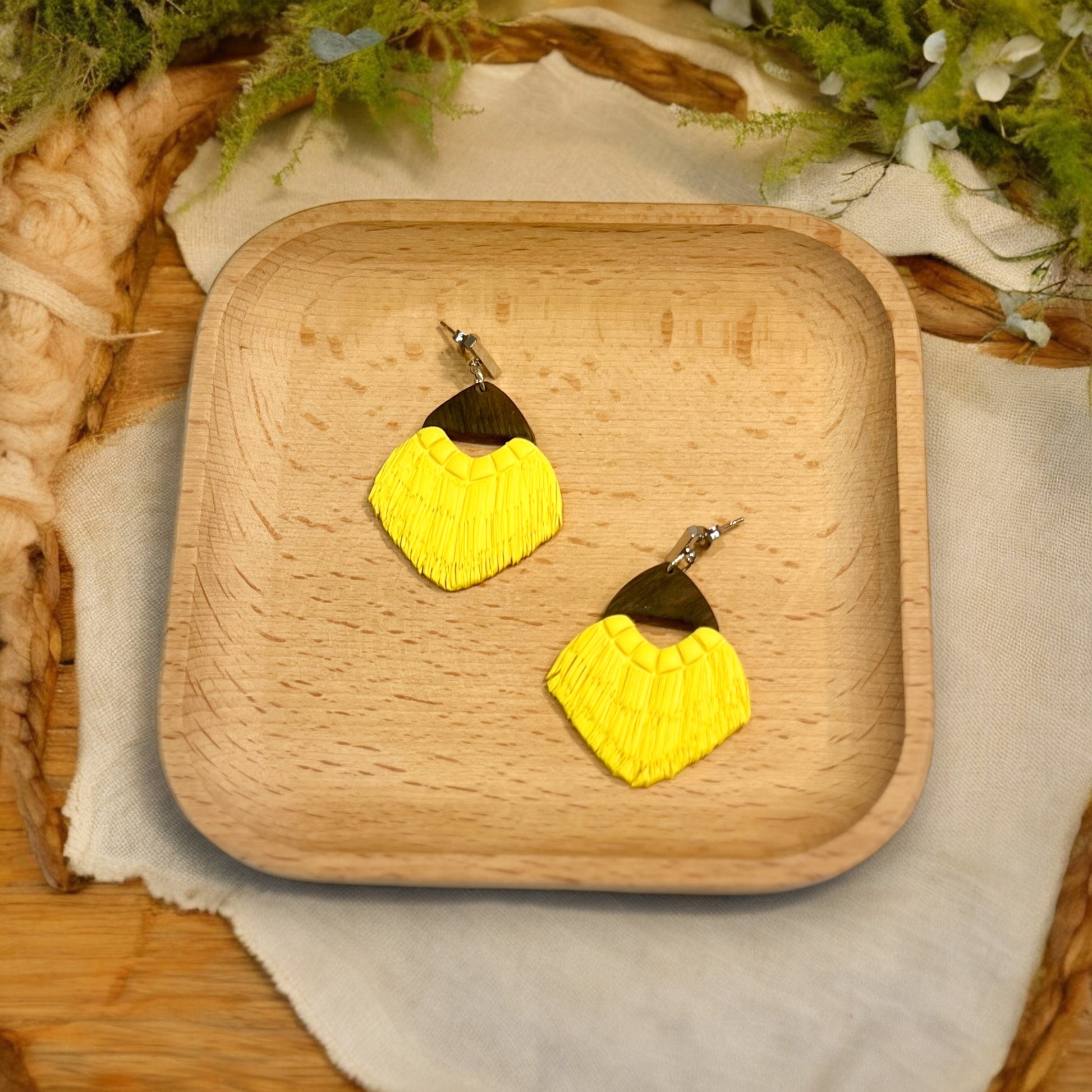 Bright yellow fan-shaped fringe dangle earrings with a wooden top, displayed on a wooden plate with rustic decor. 