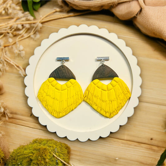Vibrant yellow earrings with intricate fringe detailing and a dark wood accent, elegantly presented on a scalloped white display plate.