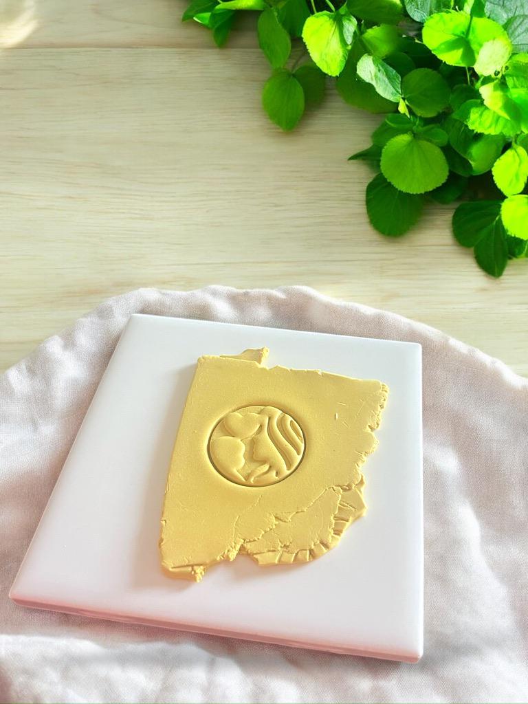 Clay slab shows circular imprint of a mother and baby design using a polymer clay cutter tool.