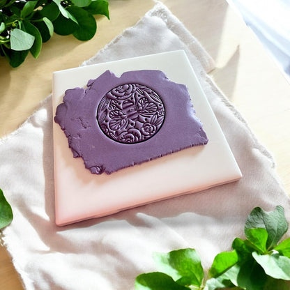 A detailed bee and floral imprint pressed into purple clay using a round polymer clay cutter, ideal for pendants or keychains
