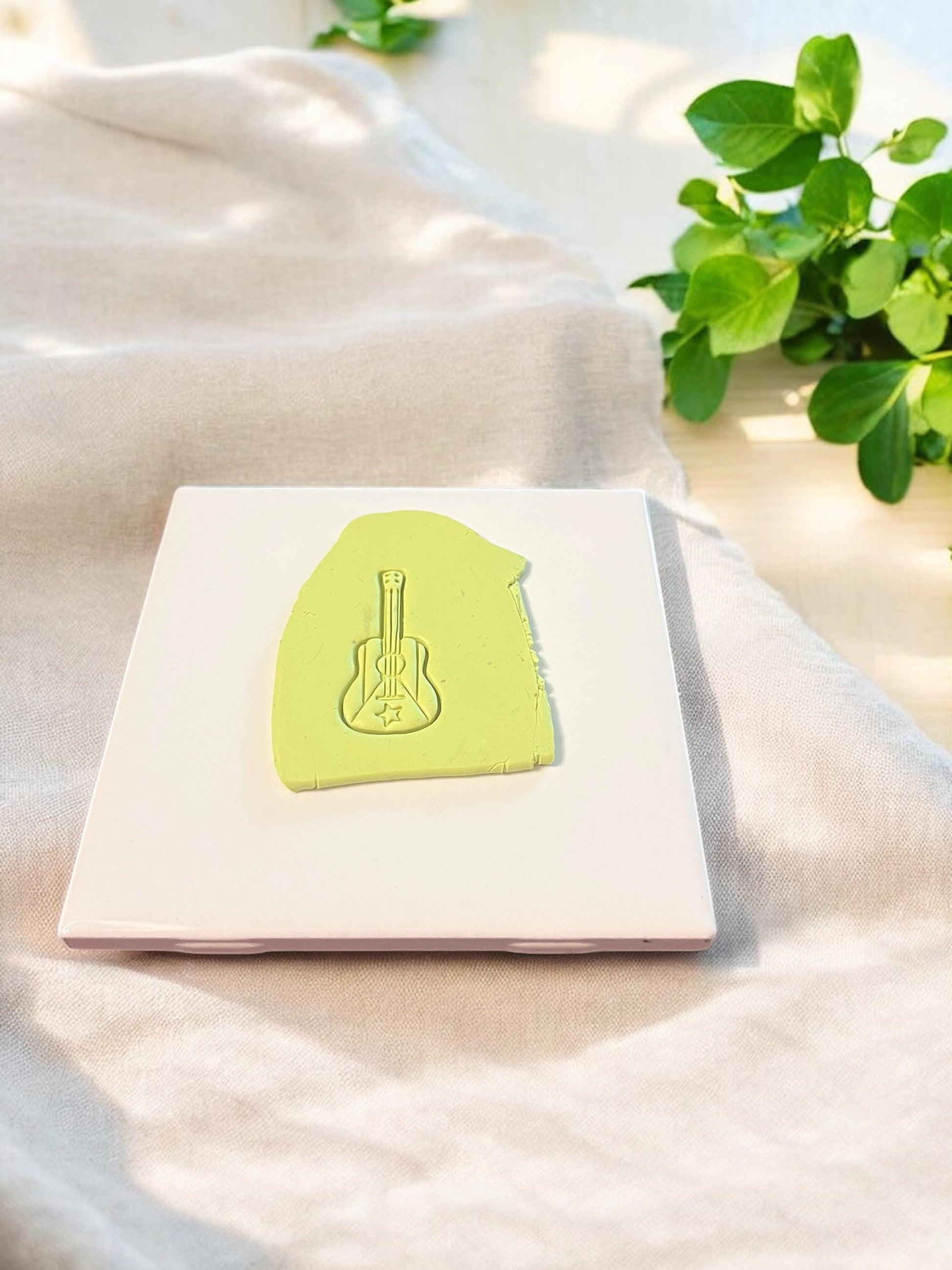 A guitar-shaped cutter imprint with a flag and star design pressed into green clay, perfect for cultural or tropical earring designs