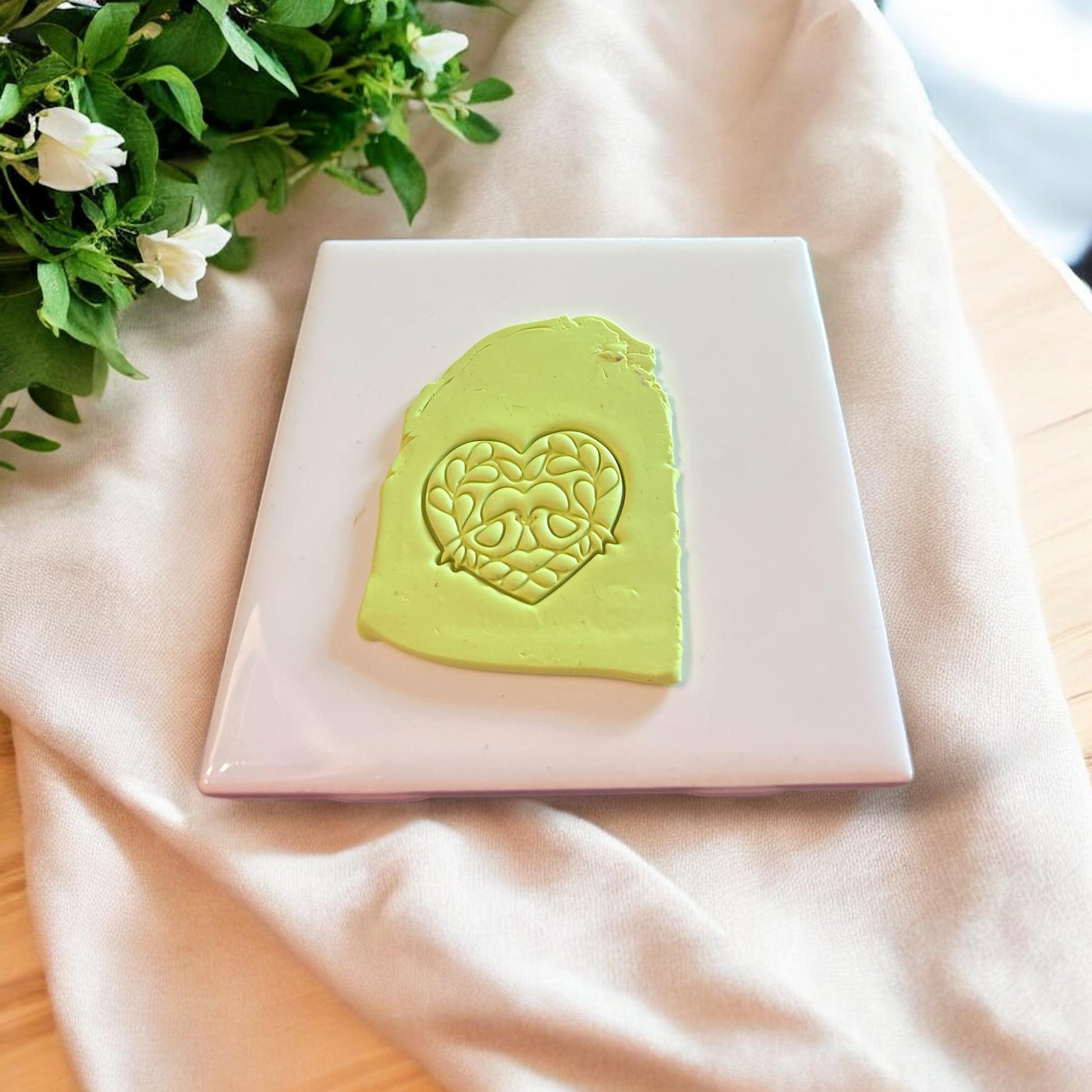 Lime green slab of polymer clay with detailed heart-shaped impression of love birds and florals.