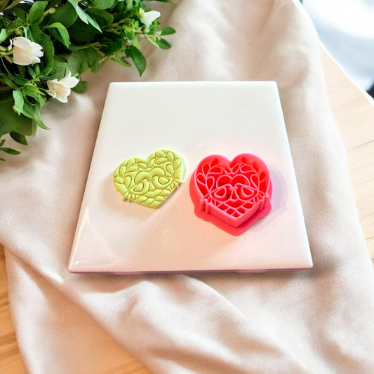 Finished heart-shaped love birds clay piece beside the matching pink 3D-printed cutter.