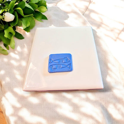 Small fish-shaped clay cutout with Parisian flair, designed for dangle earrings, placed centered on a clean ceramic tile