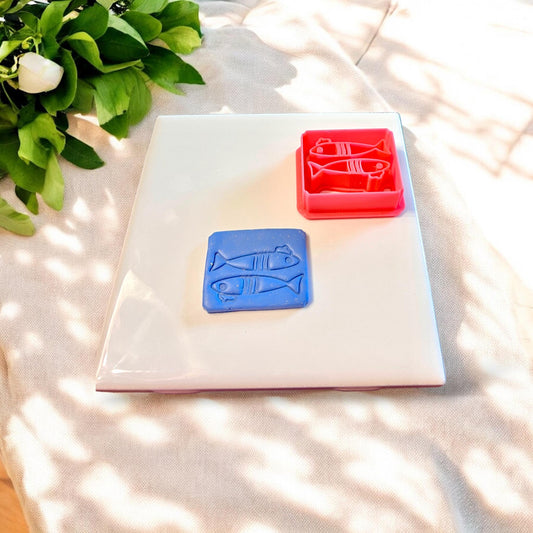 Red sardine cutter next to clay cutout, showing detailed beret hat and scale etching perfect for whimsical coastal jewelry