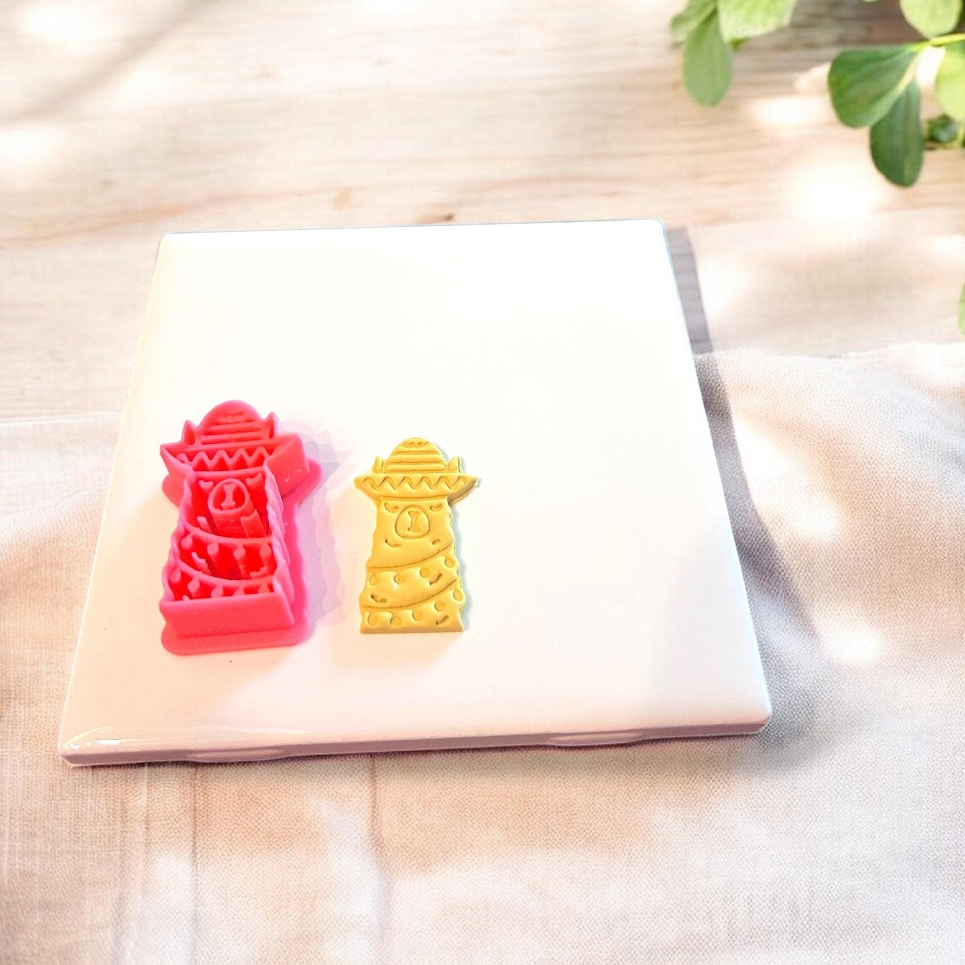 Red festive llama cutter and matching clay piece displayed together on ceramic slab with holiday props.