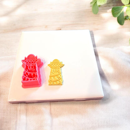 Red festive llama cutter and matching clay piece displayed together on ceramic slab with holiday props.