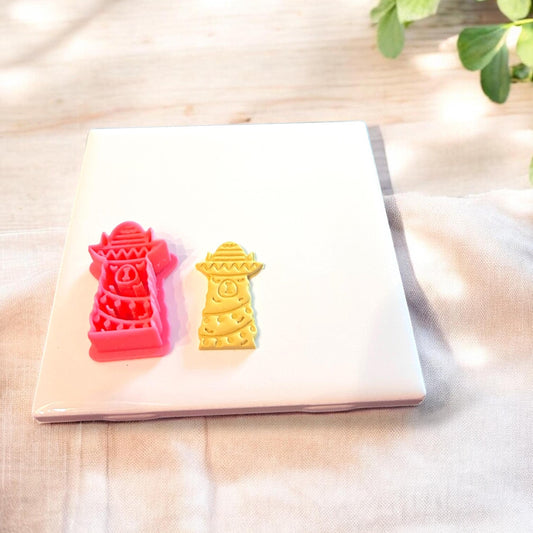 Red festive llama cutter and matching clay piece displayed together on ceramic slab with holiday props.