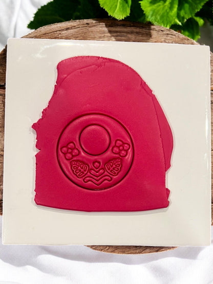 Red polymer clay slab with impression of floral folk hoop earring design, showing detailed flowers and leaves