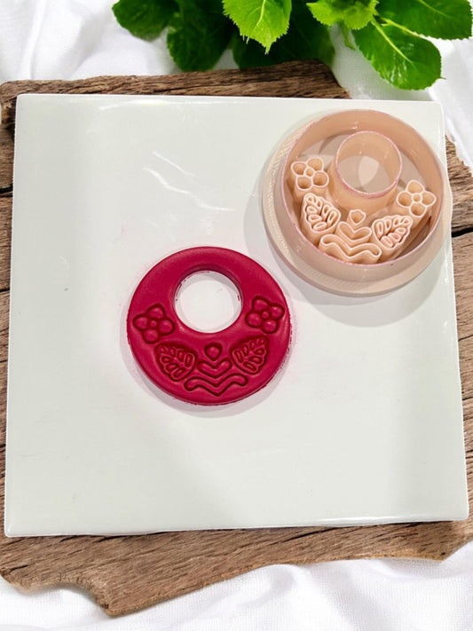 Folk floral hoop clay cutter next to completed red clay cutout with detailed flower and leaf pattern