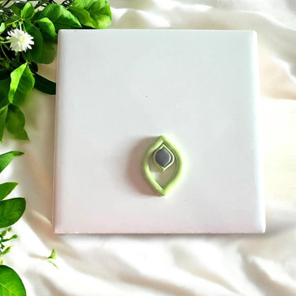 Finished green and gray jewel drop cutout pieces on a white tile surrounded by soft fabric and greenery