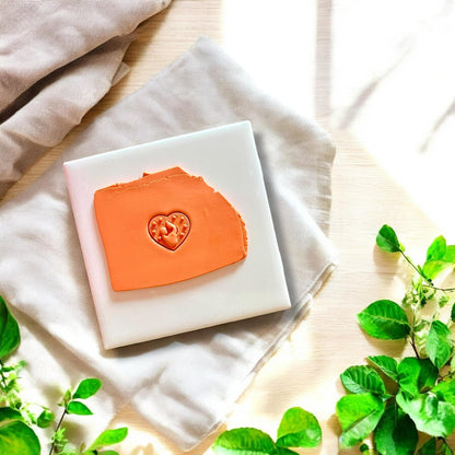 Orange clay slab with heart-shaped imprint of mother holding a baby on a white ceramic tile.