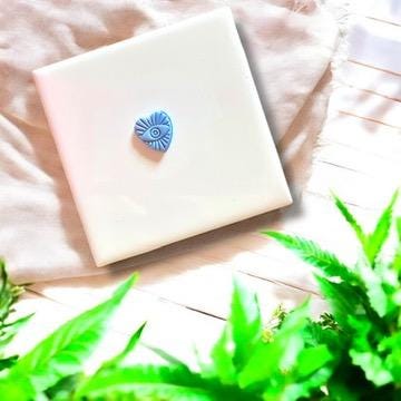 Completed evil eye heart charm in light blue polymer clay, centered on a white tile.