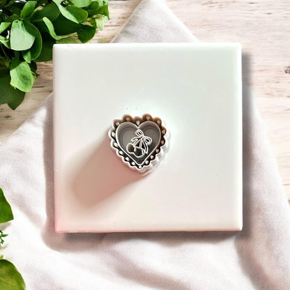 Close-up of stacked scalloped heart polymer clay cutters with cherry bow design