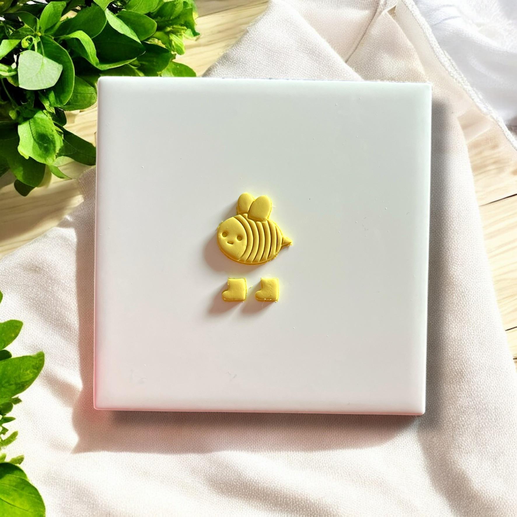 Finished yellow clay bee cutout with boots, displayed on white tile ready for baking or assembling into earrings.
