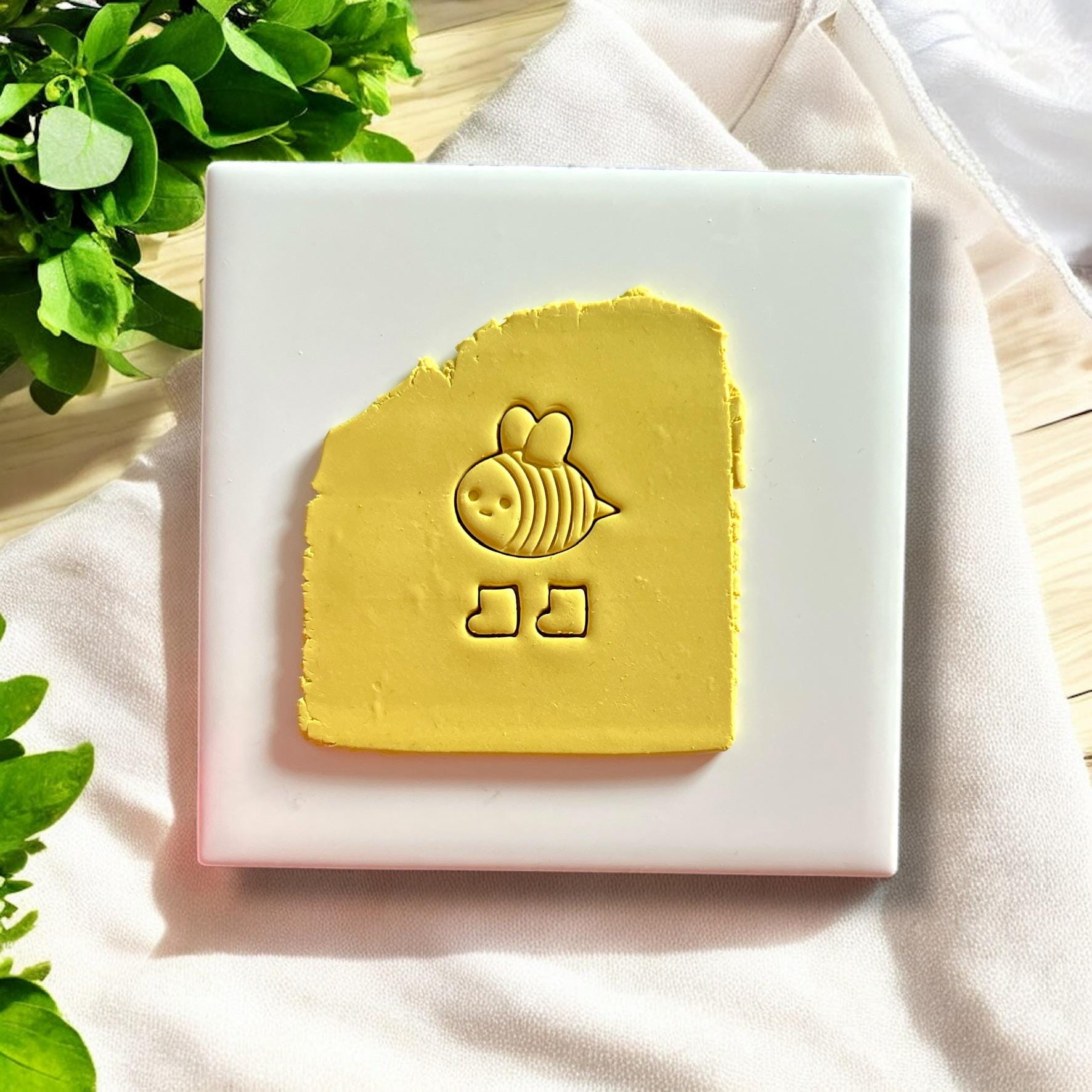Yellow polymer clay sheet with an imprint of a bee wearing boots created using a polymer clay cutter.