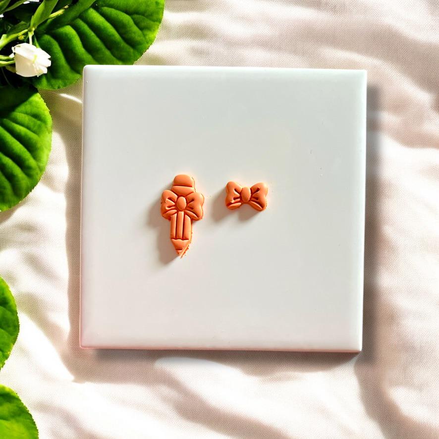 Finished pencil and bow clay pieces made using the cutter, displayed on a clean white tile