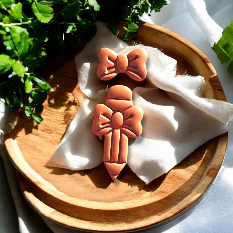 Assembled pencil and bow clay pieces displayed as potential earring design on wood background
