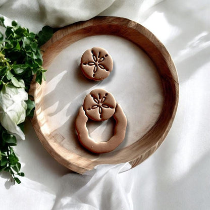 Display of assembled sand dollar dangle earrings made using the polymer clay cutter set, styled for summer creativity.