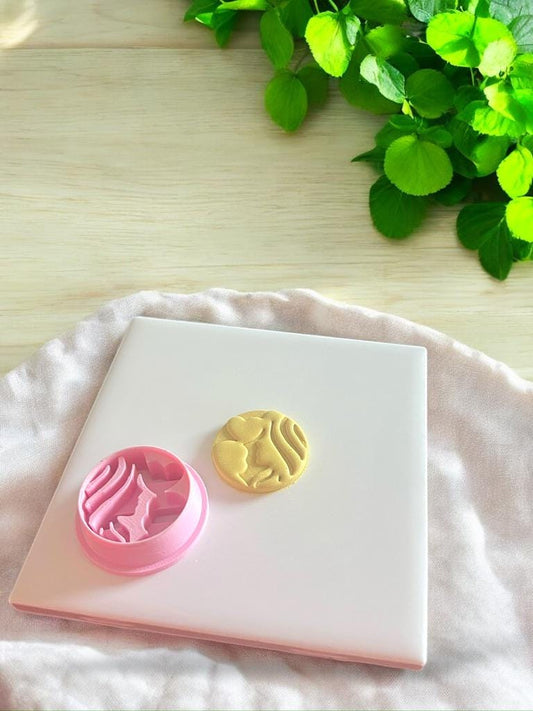 Pink circular clay cutter placed beside finished mom and baby design for earrings or charms.