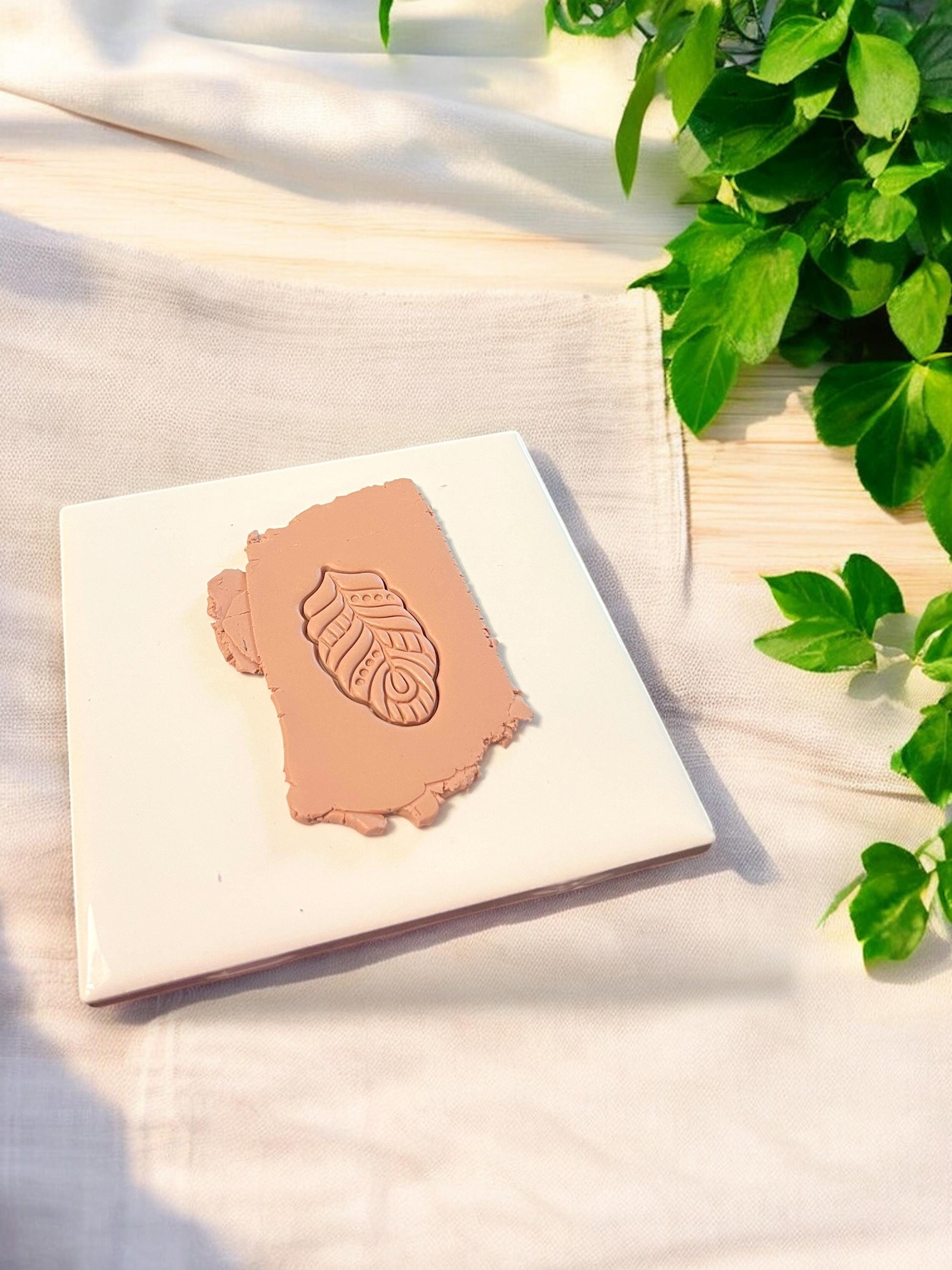 A finished clay piece shaped like a feather or abstract botanical form, made for handmade dangle earrings with etched details