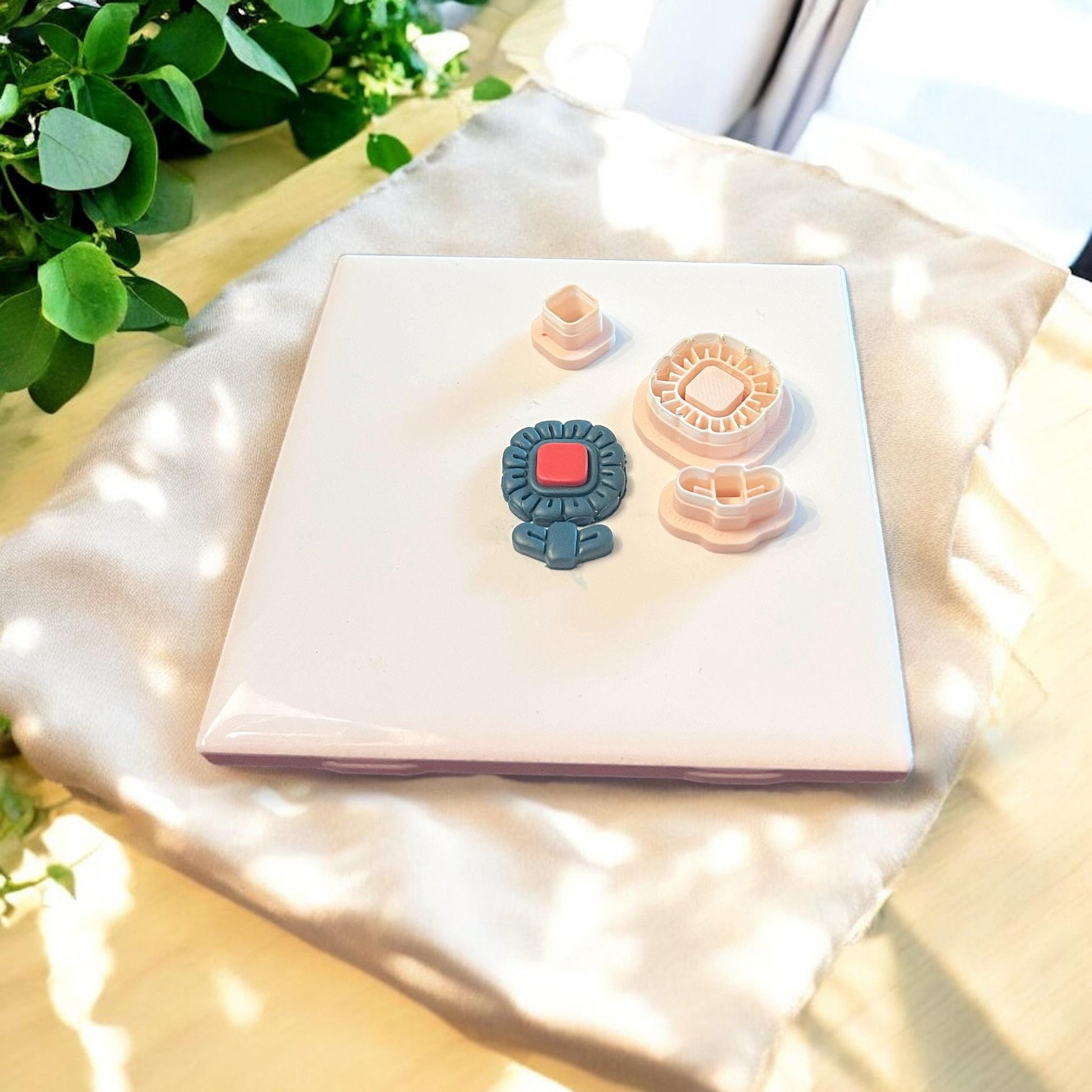 Assembled floral polymer clay piece with red gem-like center next to full 3-piece cutter set on a neutral surface