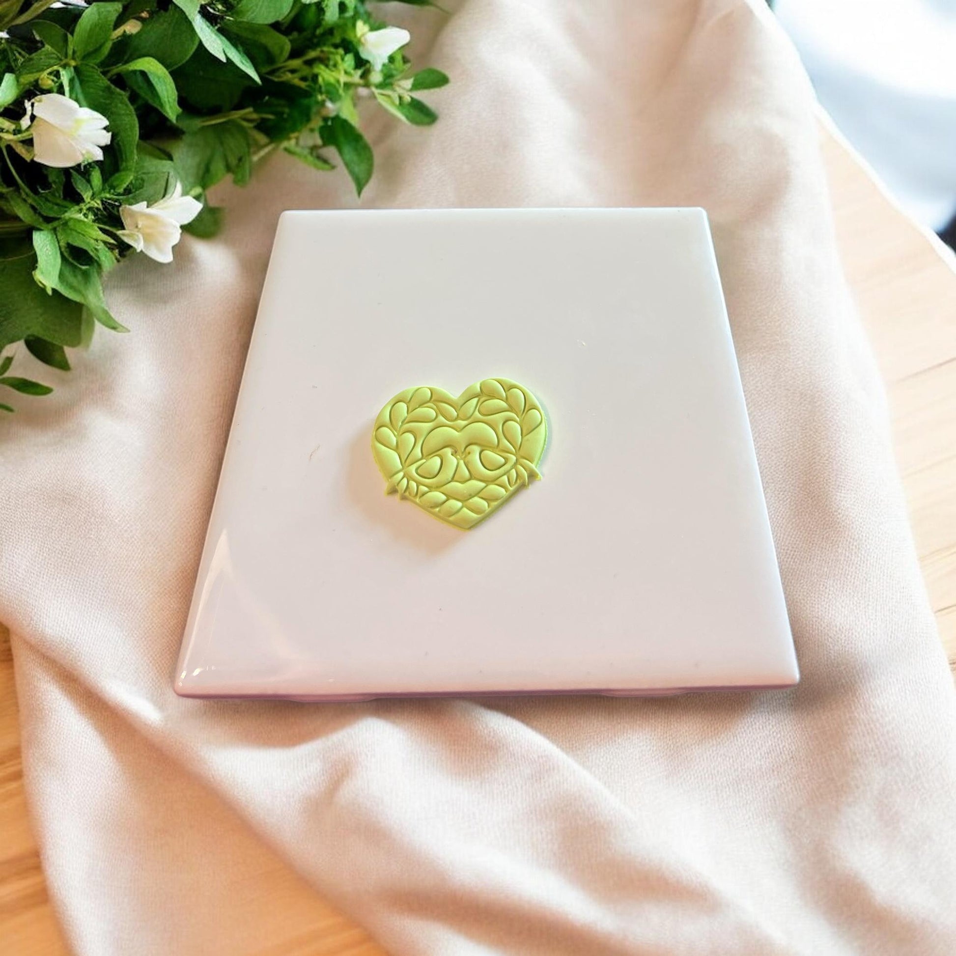 Completed clay piece in the shape of a heart with intricate love bird and floral details.