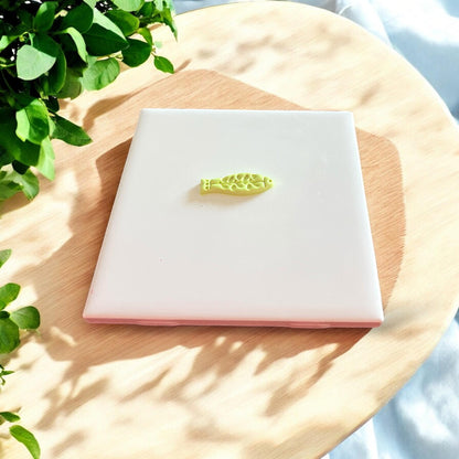 A single cut polymer clay fish piece with an intricate floral pattern placed on a clean white tile surface