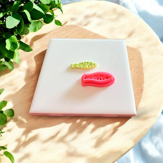 A matching polymer clay fish cutout and red 3D printed cutter shown side by side on a white tile