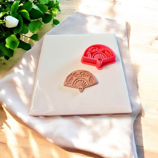 Side-by-side of red cutter and cut koi fish fan shape on white tile with soft light