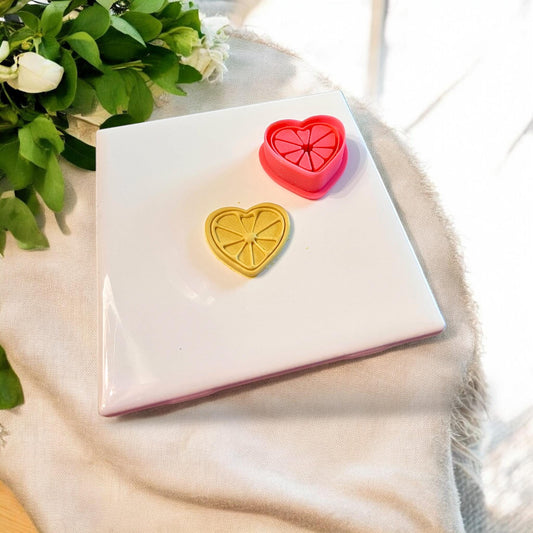 Red heart-shaped cutter shown next to citrus-shaped yellow clay impression