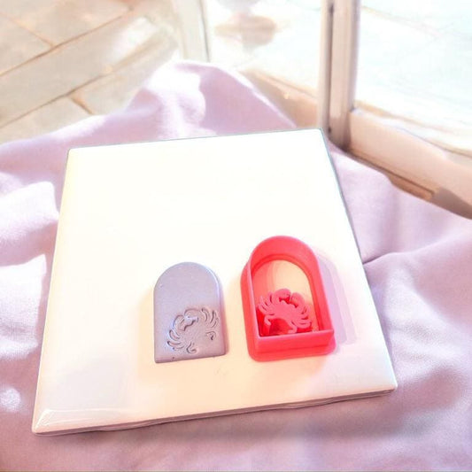 Finished crab arch clay shape and the matching pink cutter shown together on a white tile.