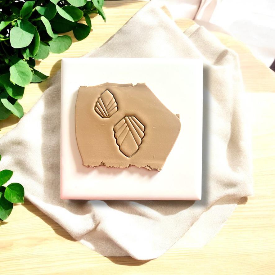 Art Deco-inspired geometric clay imprints on beige polymer clay, displayed on a white tile with fabric and greenery accents.