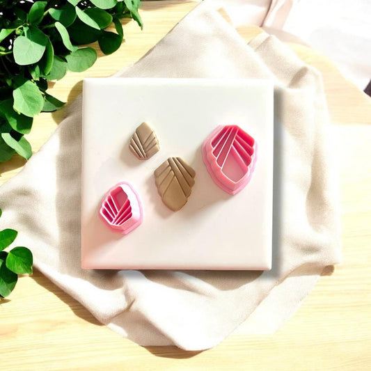 Polymer clay charms with matching Art Deco cutters in pink, displayed on a white ceramic tile with greenery.