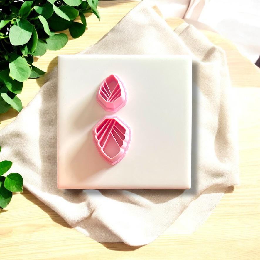 Two pink Art Deco-inspired clay cutters displayed on a white ceramic tile with a soft fabric background.
