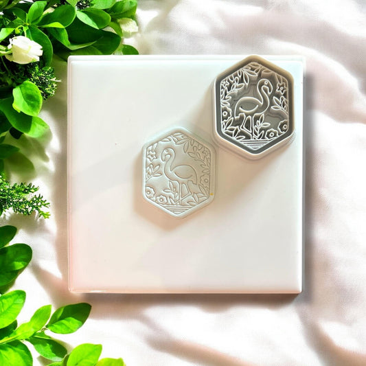 Side-by-side view of the garden flamingo clay charm and the white cutter on a white tile.
