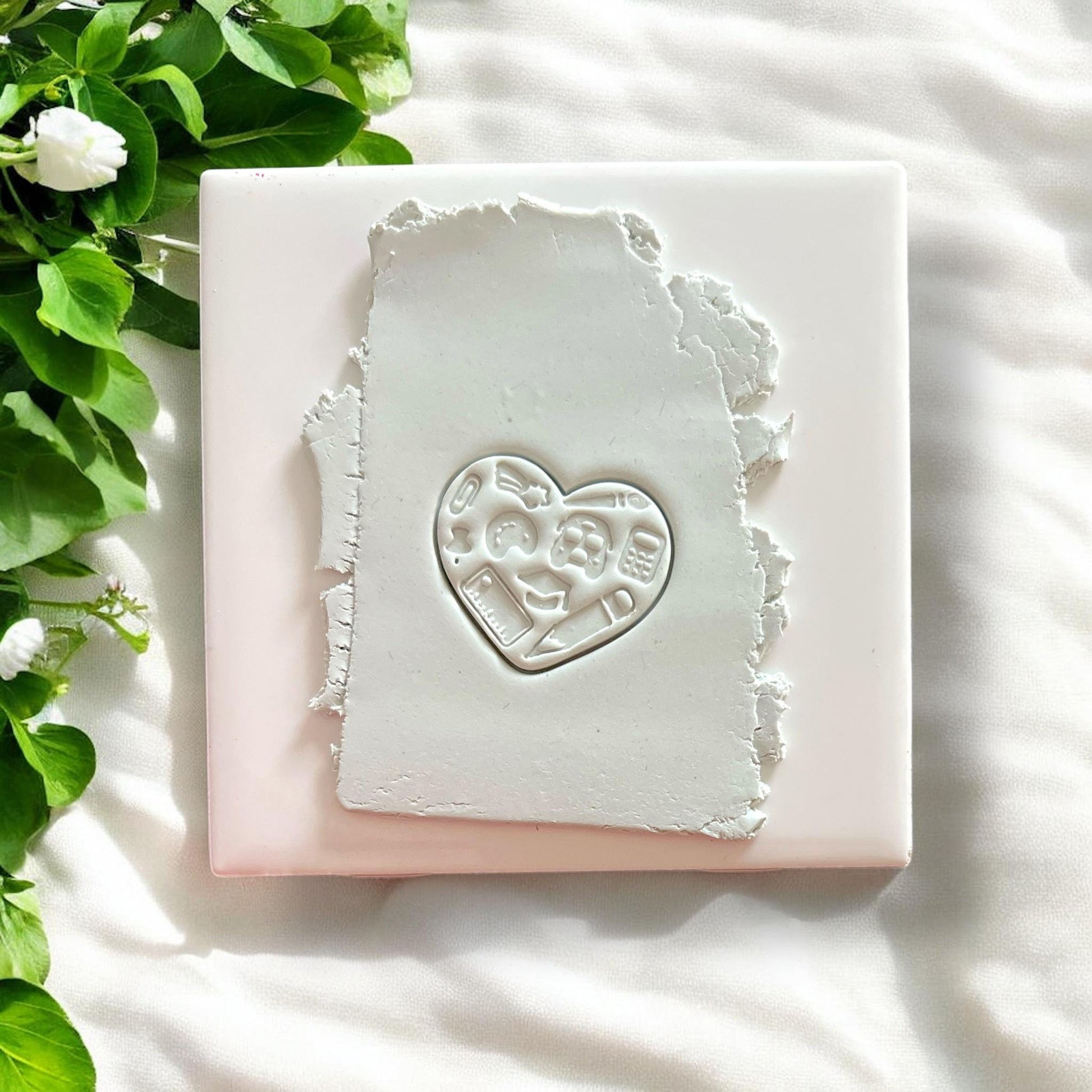 White clay slab with heart-shaped embossed school supplies, pressed cleanly with crisp detail
