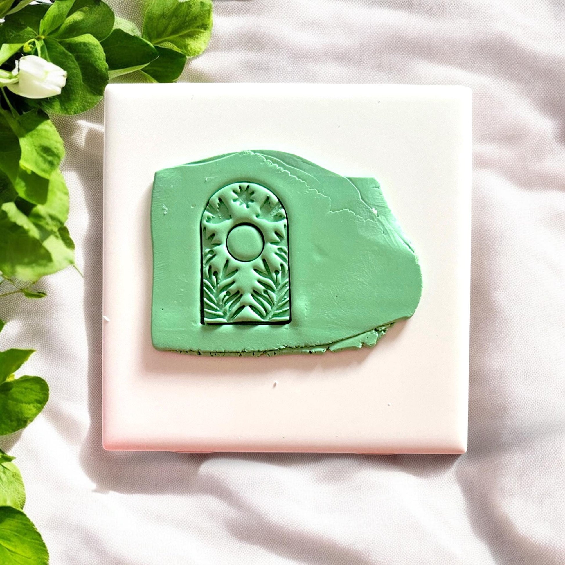 Green clay slab with deeply embossed botanical arch and sun symbol design