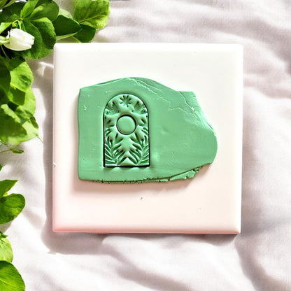Green clay slab with deeply embossed botanical arch and sun symbol design