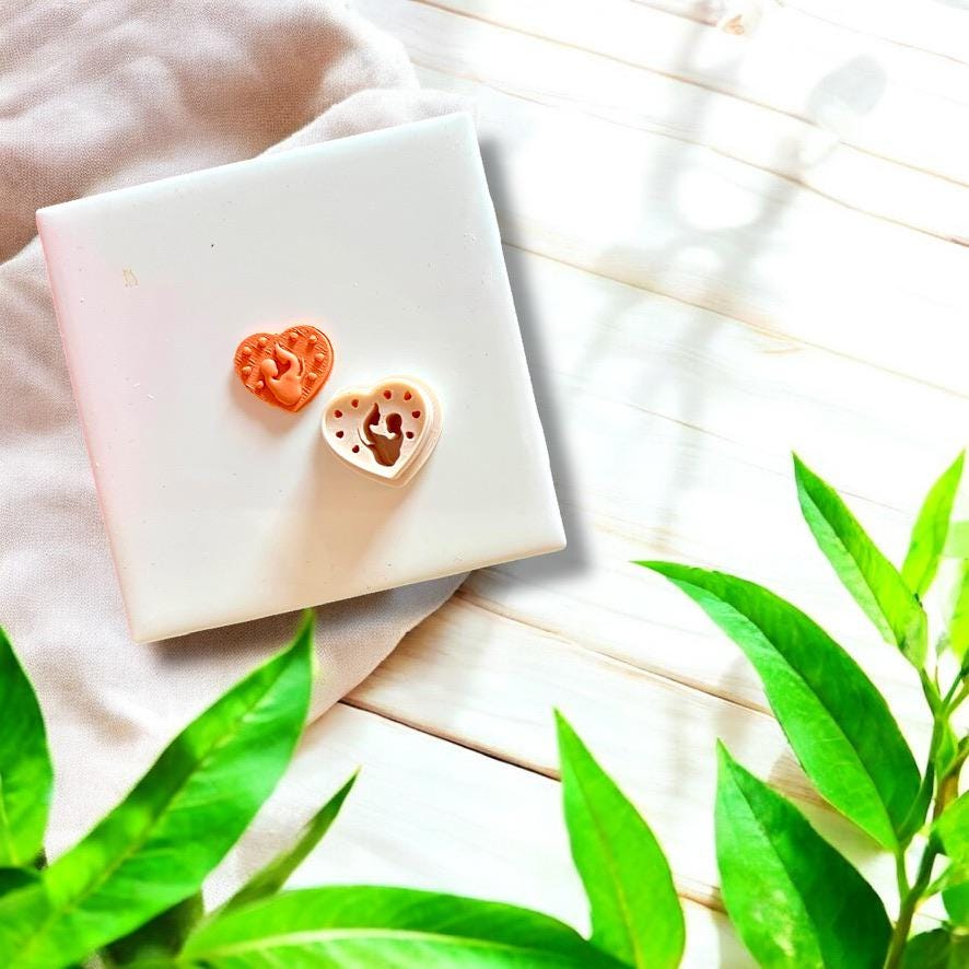 Polymer clay charm and white plastic cutter of mother and baby heart design side-by-side on tile.