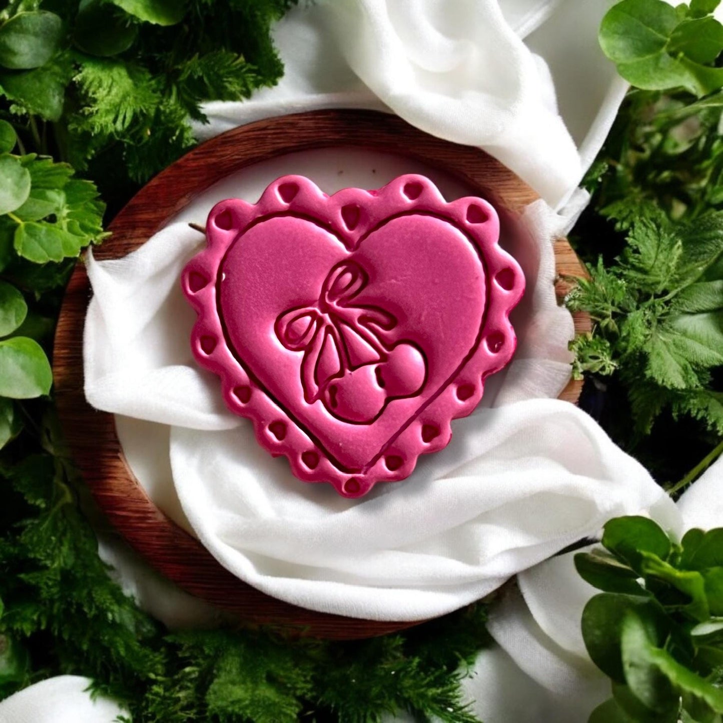 Detailed finished earring piece featuring heart, cherry, and bow staged with natural light