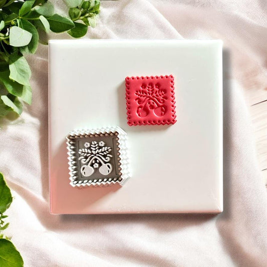 Polymer clay cutter and matching clay stamp result of cherry design displayed side by side on a ceramic background