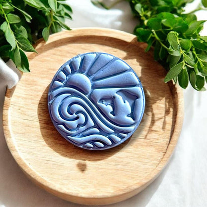 Finished dolphin and wave earring in blue clay shown on wooden tray
