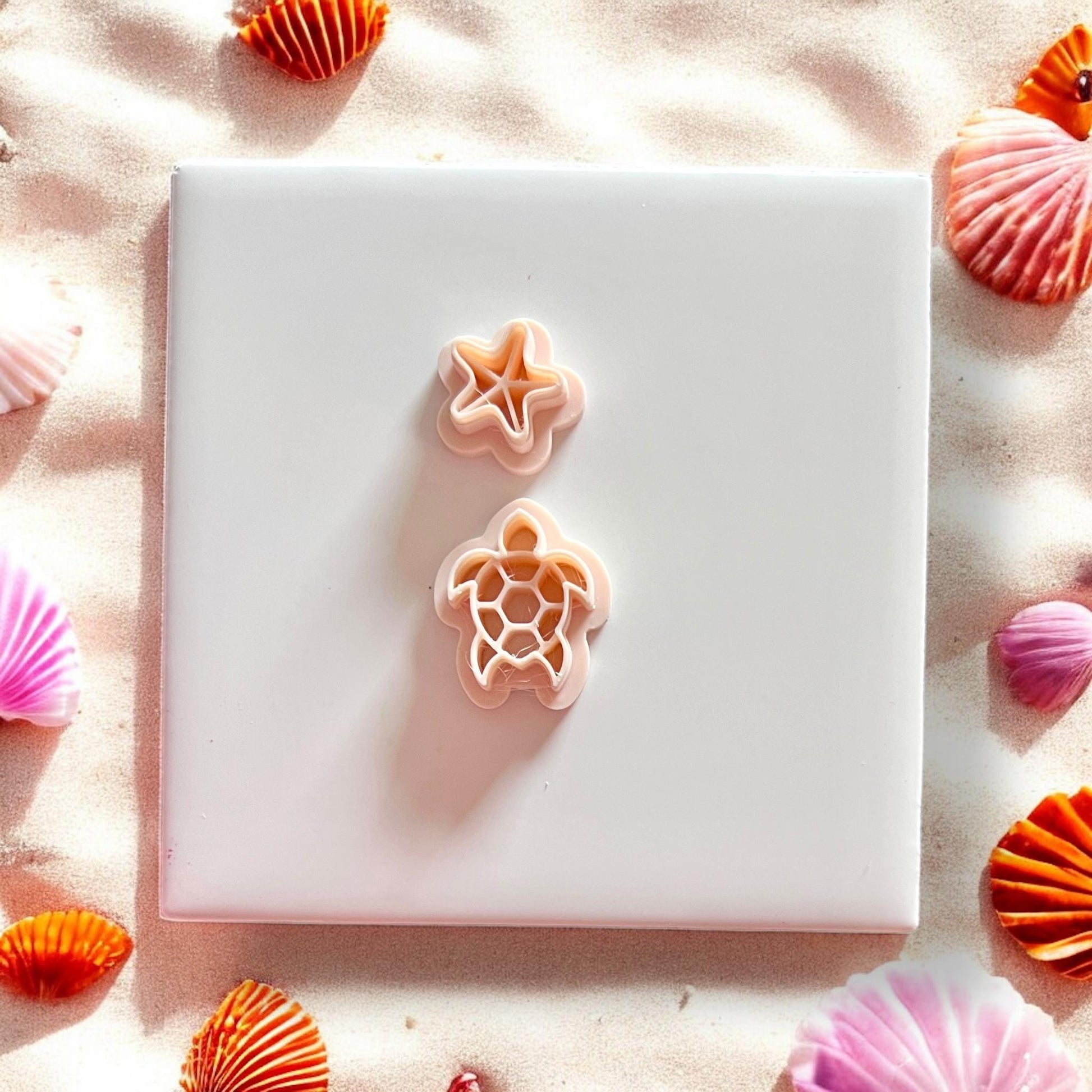 Sea turtle and starfish shaped clay cutters on white background with seashells