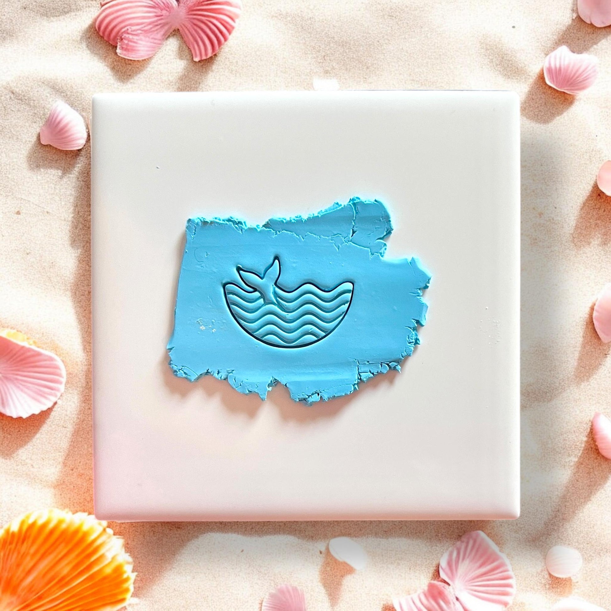 Whale tail and wave design pressed into blue clay on white tile