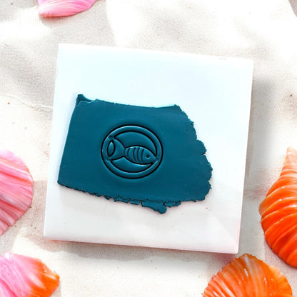 Blue clay slab with a fish inside a circle pressed into it