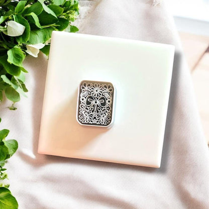 Large coquette bow and floral motif imprint on pink polymer clay, styled beautifully with greenery on a soft fabric backdrop.