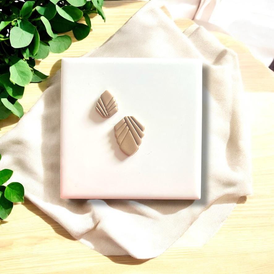 Beige polymer clay charms with Art Deco design, displayed on a white tile surrounded by soft fabric.