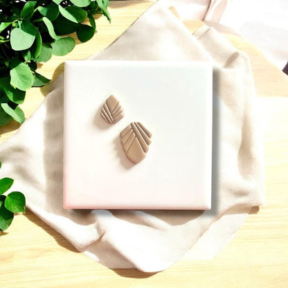 Beige polymer clay charms with Art Deco design, displayed on a white tile surrounded by soft fabric.